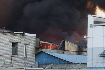 Wall Mural - Massive large blaze fire in the city, blazing warehouse factory, storage building is burning, firefighters team putting out the fire, firemen on duty, extinguish the fire, arson, burning house damage