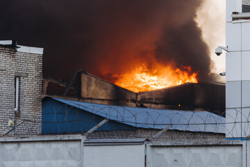 Wall Mural - Massive large blaze fire in the city, blazing warehouse factory, storage building is burning, firefighters team putting out the fire, firemen on duty, extinguish the fire, arson, burning house damage