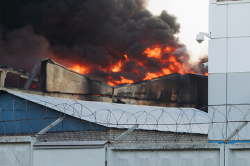 Wall Mural - Massive large blaze fire in the city, blazing warehouse factory, storage building is burning, firefighters team putting out the fire, firemen on duty, extinguish the fire, arson, burning house damage