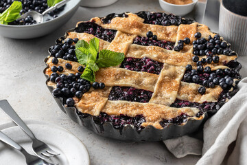 Delicious Homemade Blueberry Pie with mint on gray table with plates and cutlery