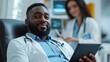 © Rajiv - Black Businessman Donating Blood For People In Need In Bright Hospital. Female Nurse With Tablet Computer Coming In To Check Progress And Well-Being Of Donor. Donation For Heart Surgery