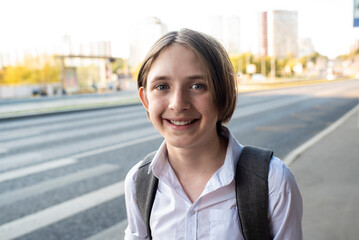 Portrait of smiling 12 year old boy in white shirt with backpack on his way to school.	