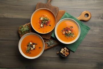 Delicious pumpkin soup in bowls, spices and pieces of bread on wooden table, top view