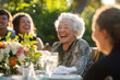 © Kien - Elderly friends laughing at an outdoor dinner table, with white hair and gray attire.