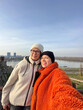 © satura_ - Joyful couple mother and daughter takes a selfie against a scenic river backdrop in autumn, warm outfits and happy expressions. Social networks and blogger concept