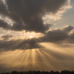 Wall Mural - A cloudy sky with the sun partially hidden behind the clouds, with sunbeams breaking through and illuminating the scene below in soft golden light
