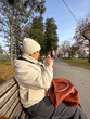 © satura_ - Woman taking a photo in a park on a sunny autumn day, moments of leisure and connection with nature amidst fall cold scenery