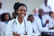 © Pete - African American female doctor stands confidently with arms crossed in busy convention center. Wearing white lab coat, stethoscope, smiling towards camera. Medical professionals surround in pro