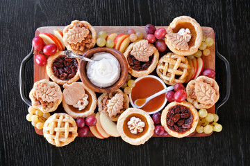 Poster - Autumn pie theme dessert board. Above view table scene against a black wood background. Pumpkin, apple and pecan mini pies, with whipped cream, caramel and fruit.