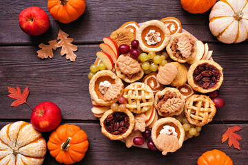 Poster - Autumn theme dessert board. Top view table scene against a dark wood background. Pumpkin, apple and pecan mini pies, cookies, pumpkin rolls and fruit.