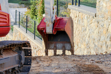 Excavator bucket digs the ground nearby. Red bucket - excavator ripper. Construction equipment.