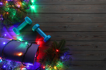 Poster - Dumbbells, mat, fir tree branches and Christmas lights on wooden table, flat lay. Space for text