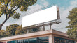 © Bockthier - An empty huge poster mockup on the roof of a mall, white template placeholder of an advertising billboard on the rooftop of a modern building framed by trees