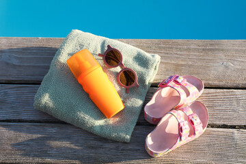 Wall Mural - Stylish sunglasses, shoes, towel and sunscreen on wooden deck near outdoor swimming pool, top view