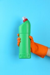 Poster - Woman holding toilet cleaner in bottle on light blue background, closeup