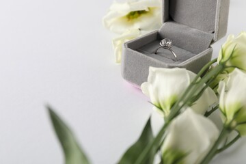 Poster - Beautiful ring with gemstone in box and flowers on white background, closeup