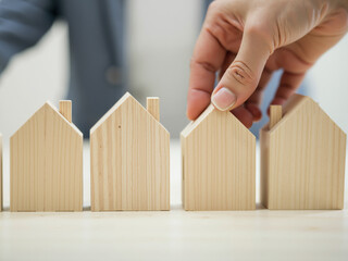 Wall Mural - building houses concept. a hand touching one of several wooden model houses on a table.