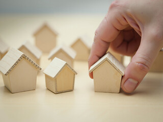 Wall Mural - building houses concept. a hand touching one of several wooden model houses on a table.