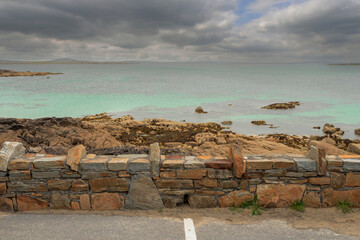 A rocky shoreline with a wall of stone and a parking lot in the foreground. The sky is cloudy and the water is blue. Dog bay, county Galway, Ireland. Dramatic cloudy sky. Popular tourist area