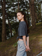 Wall Mural - Young woman standing outdoors in casual attire, gazing over her shoulder, showcasing a relaxed demeanor in a natural setting surrounded by greenery