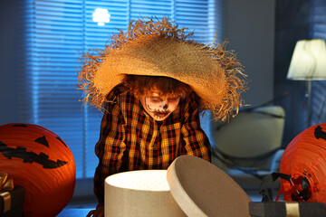 Wall Mural - Cute boy dressed like scarecrow with festive decor and gift boxes indoors at night. Halloween celebration