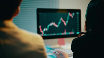 Poster - Business professionals working late in the office analyze stock market data displayed on a computer monitor, focusing on charts and graphs to inform investment strategies