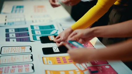 Poster - User experience designers are working together to arrange mobile application interface designs. They are moving around different pieces of paper on a table
