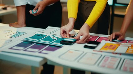 Poster - Ui designers collaborate by moving cards on a table, crafting an optimal user experience for an upcoming mobile application. Creativity and teamwork drive the design process