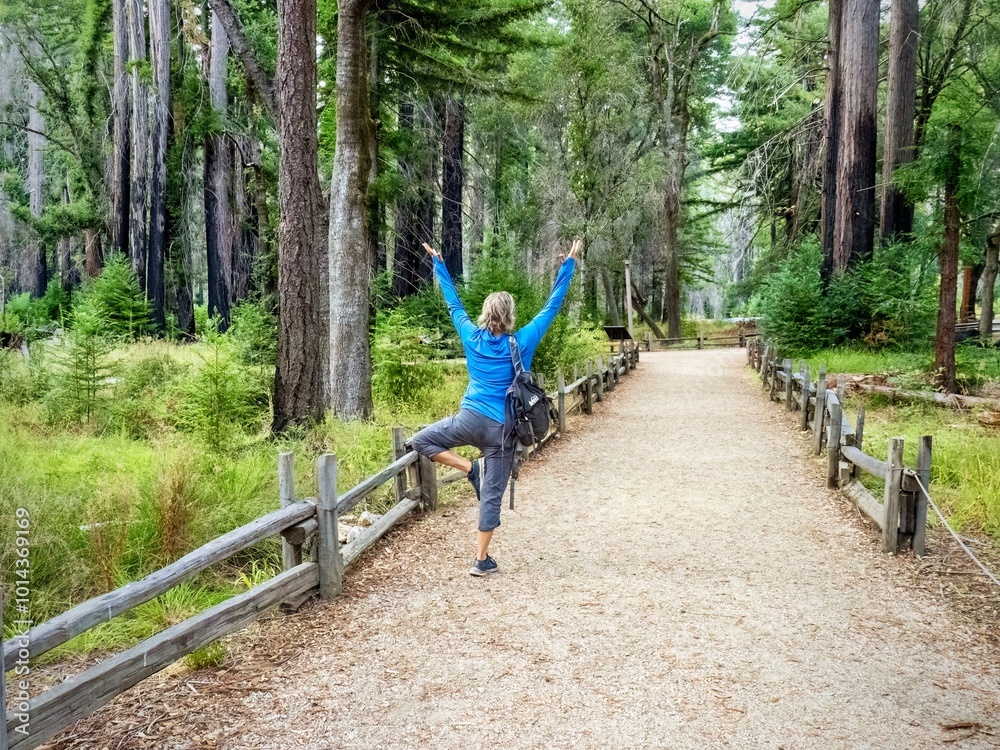 Rear view of a woman raising her arms in the yoga tree pose, while on a ...