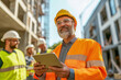 © Six Hen Media - A construction manager smiling while using a tablet on a building site with workers in helmets.