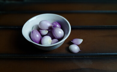 Shallots or red onion peeled on bowl with wood background