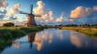 © aanu - Large traditional stone windmill wooden blades standing beside a calm river surrounded by green fields and blue sky clouds in the background
