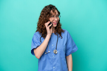 Young nurse caucasian woman isolated on blue background keeping a conversation with the mobile phone with someone