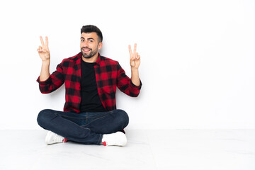 Young handsome man sitting on the floor showing victory sign with both hands