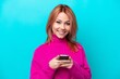 © luismolinero - Young Russian woman isolated on blue background sending a message with the mobile