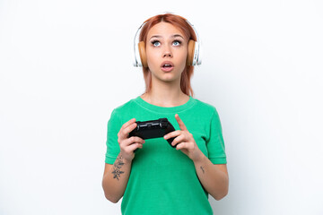 Young Russian girl playing with a video game controller isolated on white background looking up and with surprised expression