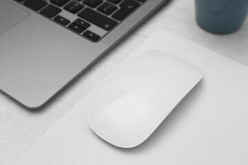 Computer mouse with mousepad and laptop on light wooden table, closeup