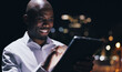 © LuxeShutter24/peopleimages.com - Night, business and black man with tablet, city and typing with internet, social media and connection. Person, evening and employee with tech, chatting and message to contact, network and texting