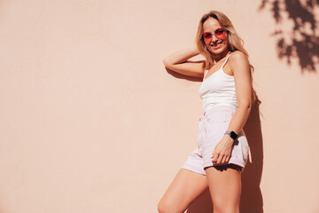 Young beautiful smiling hipster woman in trendy summer shorts and top white t-shirt. Carefree woman posing in the street near wall at sunset. Positive model outdoors. Cheerful and happy