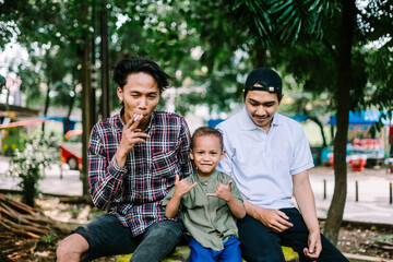 Two Southeast Asian men, close friends, chatting with one of their friend's child,