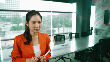 Professional young beautiful businesswoman thinking while standing at glass board with colorful sticky notes with marketing idea written. Portrait of project manager looking at mind map. Manipulator.