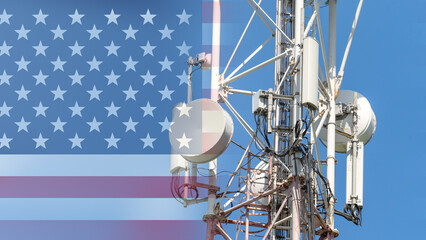 A cell phone tower is shown with the American flag in the background. The tower is surrounded by wires and is located in the middle of the image