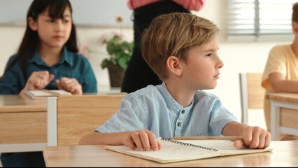 Caucasian boy looking at blackboard while diverse skilled student learning at school and taking a note. Smart child in casual cloth sitting in front of blackboard while children doing test. Pedagogy.