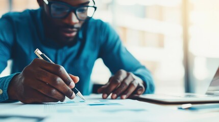 Poster - A focused individual works on a project, writing notes while using a laptop, embodying productivity and determination in a bright, modern workspace.