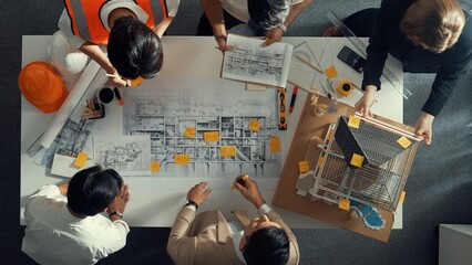 Top down view of skilled engineer team compare between blueprint and house plan. Aerial view of group of architect or designer discussing and point note to brainstorm about blueprint. Alimentation.