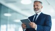 © BoOm - Smiling businessman holding tablet, modern office setting, professional attire, confident and engaged.