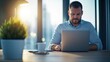 © BoOm - A professional man working on a laptop in a modern office with a plant and a coffee cup on the desk.