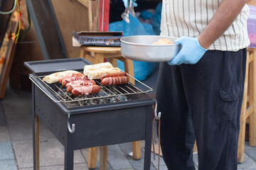 Horizontal street photo. Chef fries sausages on grill. Man cooking meat. Tbilisoba holiday fair. City Day. Kitchen on street cafe. Food festival. Concept of healthy food, sale. Cook. Tbilisi. Georgia