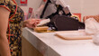 © Mdisk - Woman in floral dress stands at vibrant checkout counter, thoughtfully holding card while preparing to finalize her order at bustling food outlet
