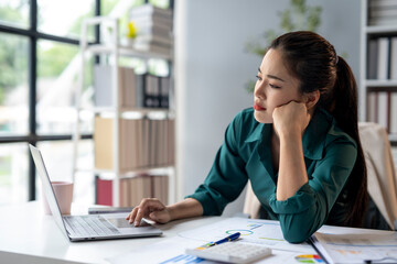 Wall Mural - A woman is sitting at a desk with a laptop open in front of her